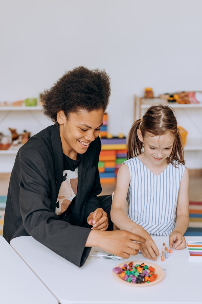 Smiling teacher assists a young girl with a colorful learning project indoors.